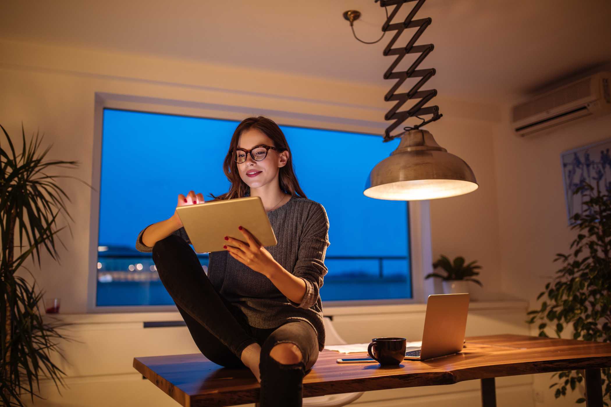 A young woman sitting on the table with her tablet in her hand.