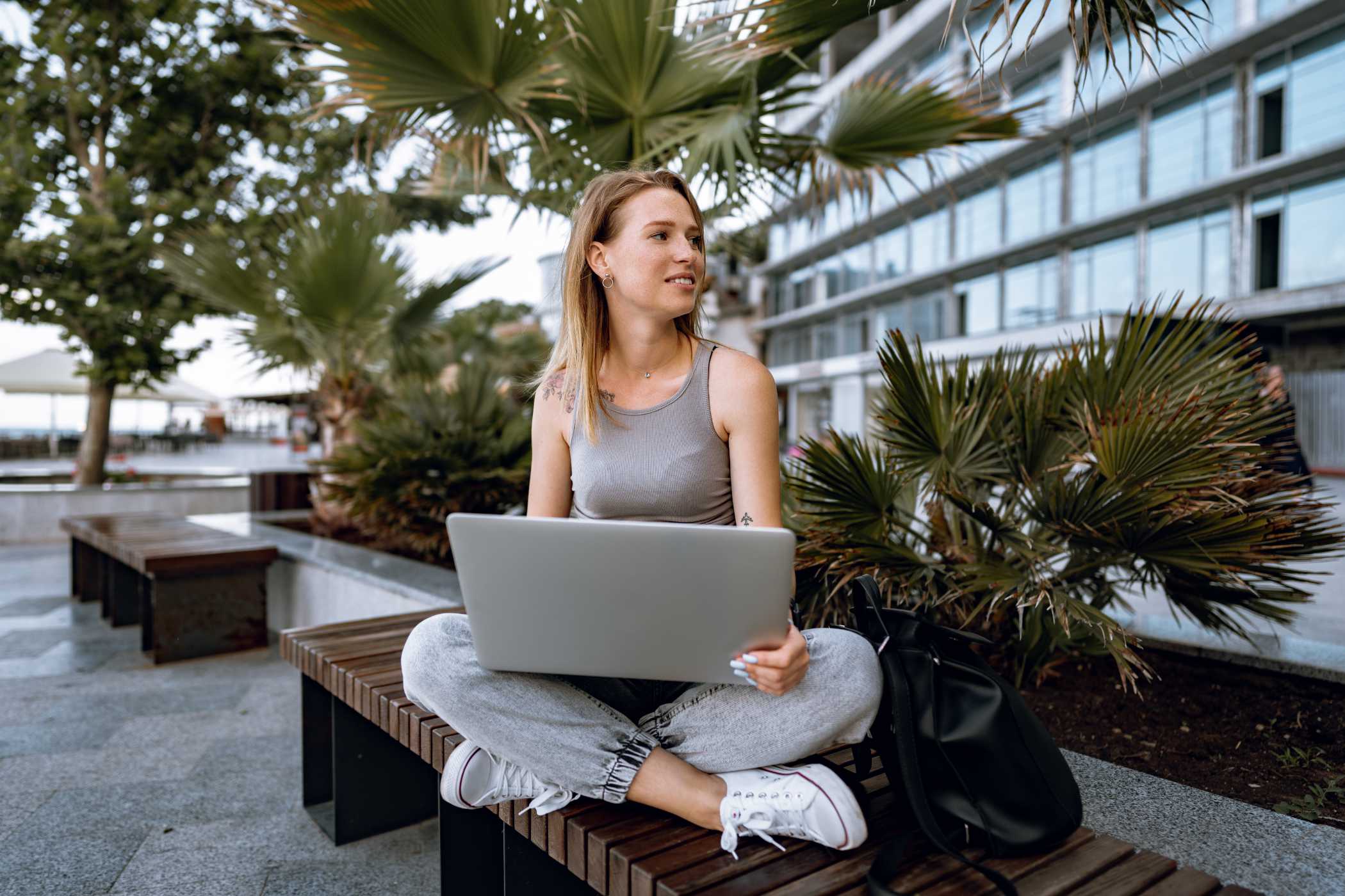 Young beautiful casual woman working on a laptop sitting on the bench in the street in summer