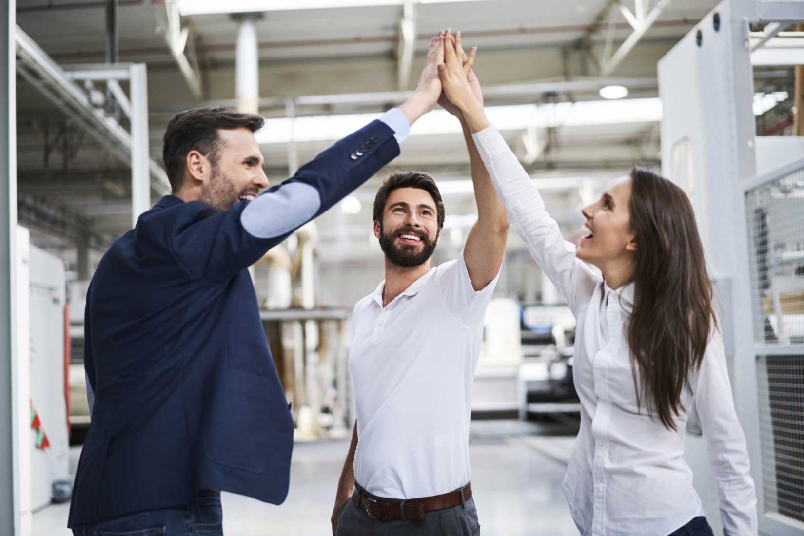 Happy businessman and employees high fiving in a factory